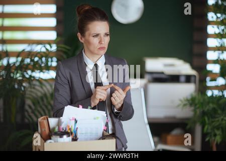 Nuovo lavoro. lavoratrice moderna in moderno ufficio verde in abito da lavoro grigio con effetti personali in scatola di cartone. Foto Stock