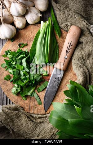 Tagliando le fresche foglie d'aglio selvatico dell'orso biologico su un asse di legno con un coltello da vicino. Fotografia gastronomica Foto Stock