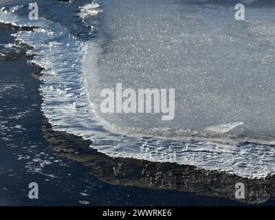 Formazioni di ghiaccio sul bordo dell'acqua alla luce del sole Foto Stock