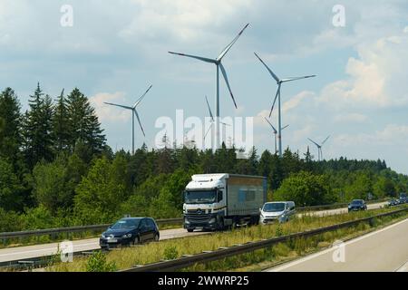 Kassel, Germania - 9 giugno 2023: Un camion percorre una strada fiancheggiata da alte turbine eoliche. Le enormi pale delle turbine girano nel vento come t Foto Stock