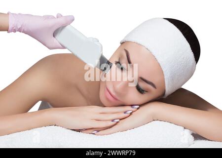 Il medico-cosmetologo rende l'apparecchio una procedura di pulizia ecografica della pelle del viso di una bella giovane donna in un salone di bellezza. COSME Foto Stock