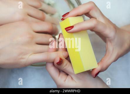 Il maestro della manicure seziona e attacca una forma di chiodo durante la procedura di estensione delle unghie con gel nel salone di bellezza. Assistenza professionale Foto Stock