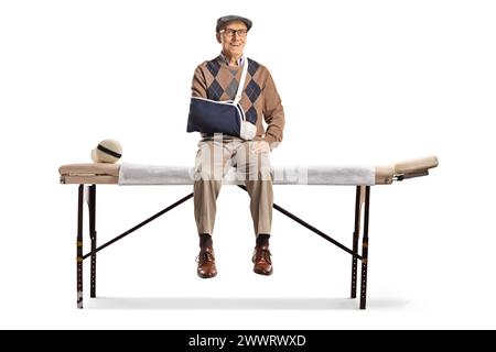 Uomo anziano con un braccio rotto seduto su un letto medico isolato su sfondo bianco Foto Stock
