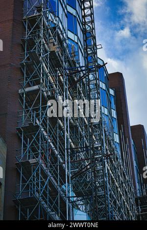 Struttura complessa con ponteggi sul lato di un edificio moderno con facciata in vetro contro un cielo blu a Leeds, Regno Unito. Foto Stock