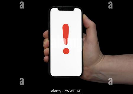 Tenere a mano il telefono che visualizza il punto esclamativo rosso su sfondo nero Foto Stock