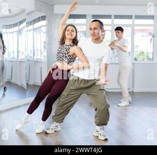 Giovani e ragazze felici in abbigliamento sportivo ballando rock and roll ballando in studio di danza durante gli allenamenti Foto Stock