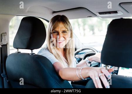 Donna felice e sorridente all'interno di un'auto che guarda i passeggeri sul sedile posteriore. Foto Stock