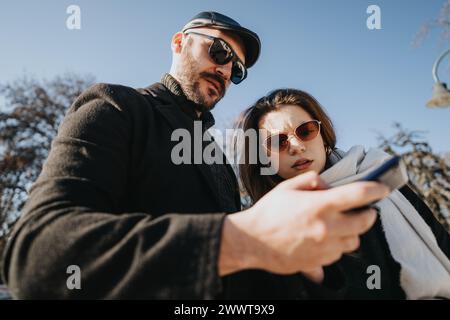 Due colleghi di lavoro si impegnano in una conversazione produttiva mentre esaminano i contenuti su uno smartphone, all'aperto in una giornata invernale intensa. Foto Stock