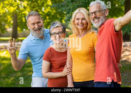 Amici anziani che posano per una foto nel parco, fanno segnali di pace e sorridono Foto Stock