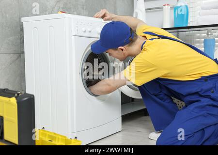 Giovane idraulico che ripara lavatrice in bagno Foto Stock