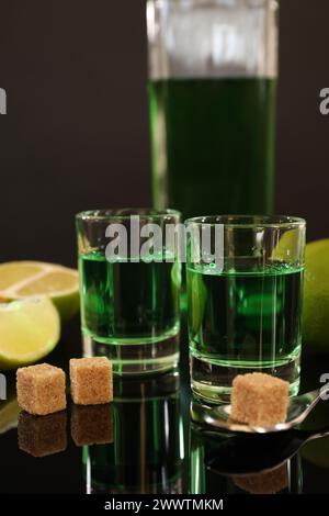 Absinthe in bicchieri da shot, zucchero di canna, lime e cucchiaio sul tavolo a specchio. Bevanda alcolica Foto Stock