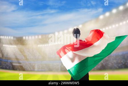 Tifoso ungherese di calcio nello stadio. Tifosi ungheresi sul campo di calcio che guardano le partite di squadra. Gruppo di tifosi con bandiera e maglia nazionale che tira Foto Stock