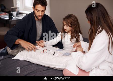 Genitori, ragazza e divertimento con carte da gioco per giocare a legare, imparare e rilassarsi con strategia in camera da letto. Padre, madre e figlia con patto Foto Stock