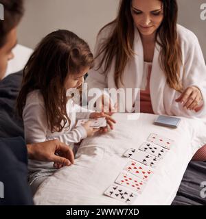 Mamma, padre e ragazza con le carte da gioco per giocare con il legame, l'apprendimento e il relax con la strategia in camera da letto. Papa', madre e figlia con patto, deck Foto Stock