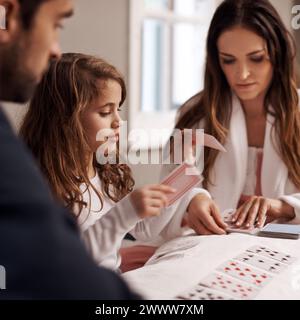 Mamma, padre e ragazza con le carte da gioco in casa con il legame, l'apprendimento e il relax con la strategia in camera da letto. Papa', madre e figlia con patto, gioco Foto Stock