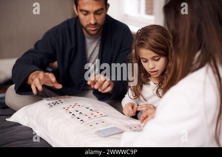 Mamma, padre e ragazza con le carte da gioco per competere con il legame, l'apprendimento e il relax con la strategia in camera da letto. Papa', madre e figlia con un accordo Foto Stock