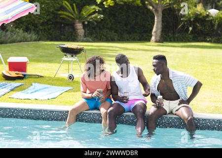 Tre diversi amici maschi si stanno godendo una conversazione in piscina Foto Stock