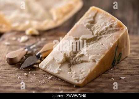 Un blocco e pezzi di parmigiano su un tagliere insieme a uno scalpello e uno spiedino. Foto Stock