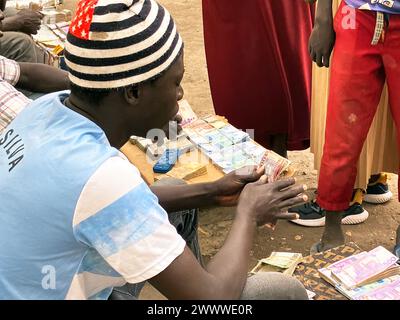 Joda, Sudan del Sud. 19 marzo 2024. Un cambiavalute al valico di frontiera di Joda nel Sud Sudan conta le banconote di un rifugiato sudanese. La lotta di potere in Sudan, in corso dalla metà di aprile 2023, ha scatenato la più grande crisi mondiale dei rifugiati, secondo le Nazioni Unite, con più di otto milioni di rifugiati. Mentre molte di queste persone cercano sicurezza dai combattimenti in Sudan, altre sono fuggite nei paesi vicini del Sudan del Sud o del Ciad. Crediti: Eva-Maria Krafczyk/dpa/Alamy Live News Foto Stock