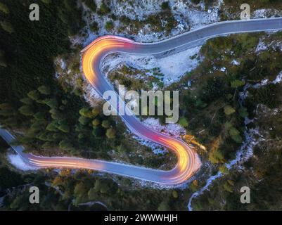 Una vista perpendicolare di una strada tortuosa con tracce di luci di passaggio per auto. Fotografia a lunga esposizione. Linee gialle e rosse, vista serale, strada di montagna. Foto Stock