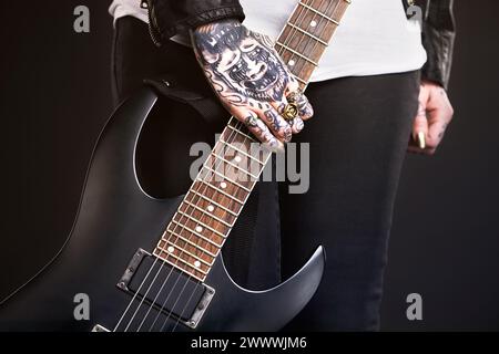 Metal, donna e chitarra su sfondo nero per la cultura punk o grunge, moda audace e gotica con primo piano. Rock star, mani e isolate in studio Foto Stock