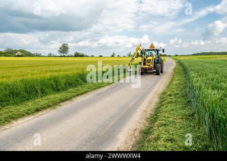 Taglio di argini lungo una strada B, manutenzione da parte di agenti del dipartimento. Argine che taglia lungo una strada B per la sicurezza di automobilisti, ciclisti e di altri Foto Stock