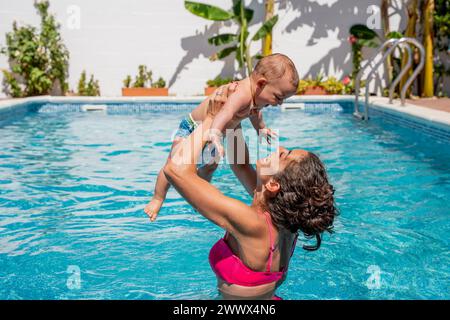 la giovane madre si diverte e ride con il suo bambino nella piscina dell'hotel mentre la tiene in braccio. curiosità, scoperta e sviluppo del bambino. se Foto Stock