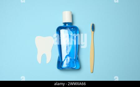 Flacone in plastica con collutorio, spazzolino da denti in legno su sfondo blu, vista dall'alto Foto Stock