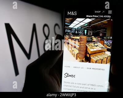Persona che detiene un cellulare con il sito web della società di vendita al dettaglio britannica Marks and Spencer Group plc davanti al logo. Messa a fuoco al centro del display del telefono. Foto Stock
