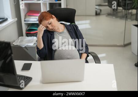 Donna incinta che dorme alla sua scrivania in ufficio. Foto Stock