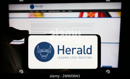 Persona che detiene un cellulare con il logo della società britannica Herald Investment Trust plc di fronte alla pagina web aziendale. Mettere a fuoco il display del telefono. Foto Stock