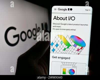 Persona che detiene lo smartphone con la pagina web della conferenza annuale degli sviluppatori Google io davanti al logo dell'azienda. Messa a fuoco al centro del display del telefono. Foto Stock