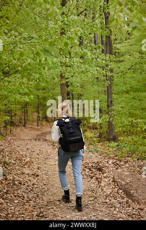 Foto retrovisiva di una donna bionda viaggiatrice con zaino in cerca di indicazioni per camminare lungo il sentiero della foresta Foto Stock