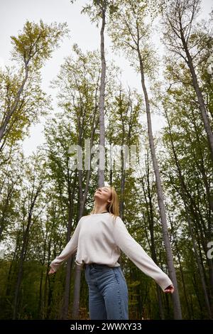 Meditare bionda in un'accogliente escursione in maglione nella foresta e godersi momenti tranquilli a occhi chiusi Foto Stock