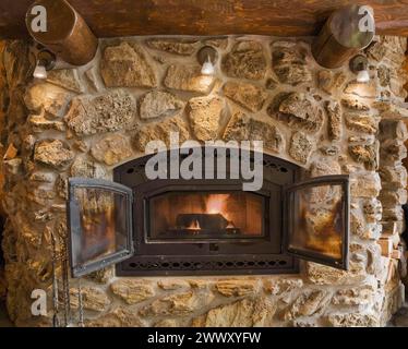 Pietra di campo illuminata e caminetto in pietra porosa nel soggiorno all'interno di una capanna in legno di cedro rosso artigianale, Quebec, Canada Foto Stock