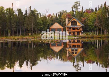 Garage e capanna in legno di abete a due piani realizzata a mano con camino in pietra e tetto in lamiera verde sul bordo del lago in autunno, Quebec, Canada Foto Stock