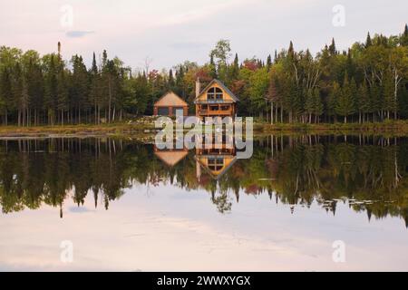 Garage e capanna in legno di abete a due piani realizzata a mano con camino in pietra e tetto in lamiera verde sul bordo del lago in autunno, Quebec, Canada Foto Stock