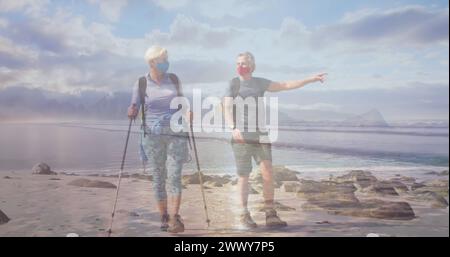Coppia di anziani caucasici in maschera per fare escursioni sulla costa, sul mare in movimento. pensionamento attivo e sano e libertà durante il concetto di pandemia di coronavirus Foto Stock