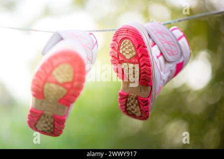sneakers rosa grigie essiccate su una corda nel giardino estivo soleggiato. Foto Stock