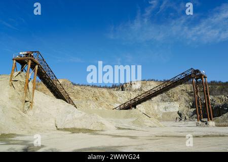 Enormi strutture metalliche arrugginite per il trasporto di rocce in una cava di dolomite, frantumazione della ghiaia, smistamento, trasporto, sfondo blu del cielo Foto Stock