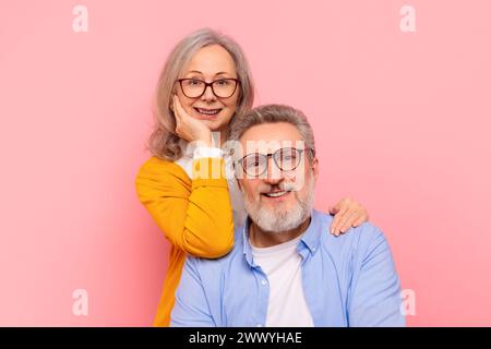 Ritratto in studio di una coppia anziana amorevole che indossa occhiali da vista, sfondo rosa Foto Stock