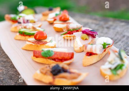 Finger food, vari canapè con verdure, prosciutto, pancetta, formaggio e olive su tavola di legno. Foto Stock