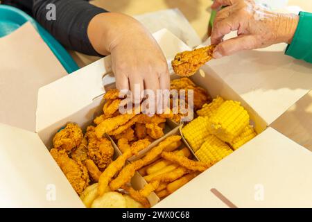 le mani di due donne prendono il cibo da una scatola di fast food con pollo, mais, patatine fritte e arepas in un'area ristoro Foto Stock