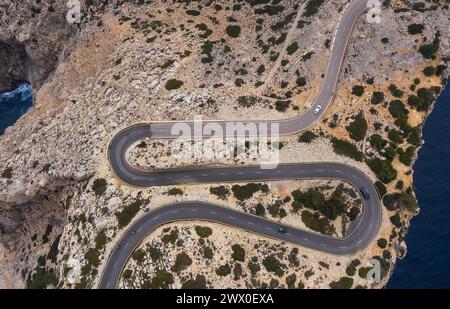 Piccola auto bianca solitaria che guida su una strada di montagna asfaltata curva a serpentina vicino al faro di Cap de Formentor con vista mare con costa rocciosa. Maiorca Foto Stock