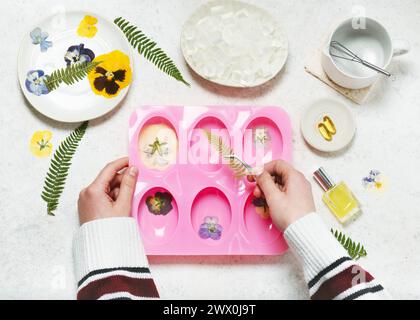 Fase 2. Mettere una foglia di felce pressata su uno stampo in silicone. Preparazione di sapone naturale per Pasqua o per la festa della mamma con i bambini. Concetto creativo fai-da-te. Vista dall'alto. Foto Stock