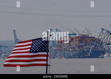 Una bandiera americana viene vista insieme ai resti di Francis Scott Key Bridge fuori Baltimora, Maryland, dopo che una nave portacontainer ha perso energia elettrica e ha colpito il ponte nelle prime ore del mattino di martedì 26 marzo 2024. Credito: Aaron Schwartz/CNP Foto Stock