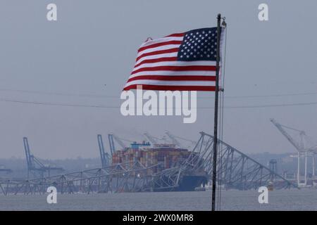 Una bandiera americana viene vista insieme ai resti di Francis Scott Key Bridge fuori Baltimora, Maryland, dopo che una nave portacontainer ha perso energia elettrica e ha colpito il ponte nelle prime ore del mattino di martedì 26 marzo 2024. Credito: Aaron Schwartz/CNP Foto Stock