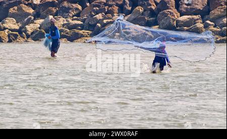 Due pescatori gettano una rete nel mare di fronte a una parete rocciosa nel Golfo della Thailandia Foto Stock