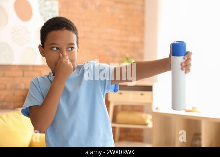 Piccolo ragazzo afro-americano disgustato dal cattivo odore usando un deodorante per ambienti in soggiorno Foto Stock