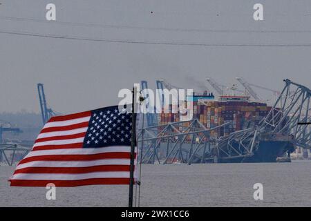 Una bandiera americana è visibile insieme ai resti del Francis Scott Key Bridge fuori Baltimora, Maryland, dopo che una nave portacontainer ha perso energia elettrica e ha colpito il ponte nelle prime ore del mattino martedì 26 marzo 2024 a Baltimora, MD, USA. Sei persone sono scomparse e presumibilmente morte dopo che una nave container ha colpito il monumento Francis Scott Key Bridge nella città americana di Baltimora. La Guardia Costiera ha detto di aver sospeso la ricerca e iniziato uno sforzo di recupero. Diversi veicoli stavano attraversando il ponte, che è lungo più di 1,6 km, quando è crollato dopo che la nave ha colpito un supporto. Dicono gli ufficiali Foto Stock